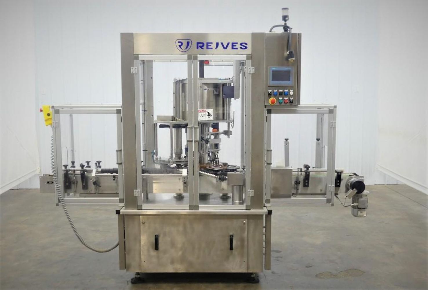 Automated stainless steel capping machine with clear safety panels, control buttons, digital display, and conveyor system in an industrial setting. The label REJVES is visible at the top front. Featured in the Quarterly Food and Beverage Packaging Equipment Auction.
