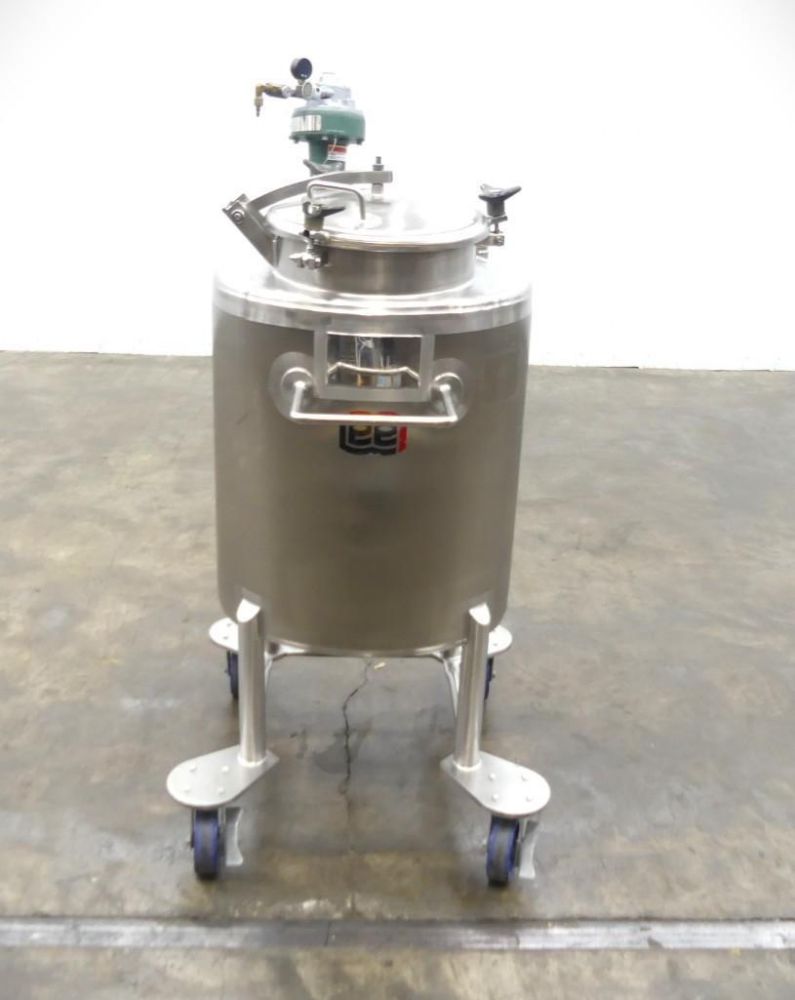 A stainless steel industrial tank with handles and a pressure gauge on top, mounted on four legs with blue caster wheels, stands on a concrete floor against a plain white background—available at the Monthly SIGMA Showroom Floor Multi-Industry Auction.