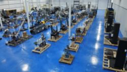 Industrial warehouse with multiple pieces of machinery organized on pallets in rows atop a bright blue floor, showcased for the Monthly SIGMA Showroom Floor Multi-Industry Auction, with white walls and support columns visible.