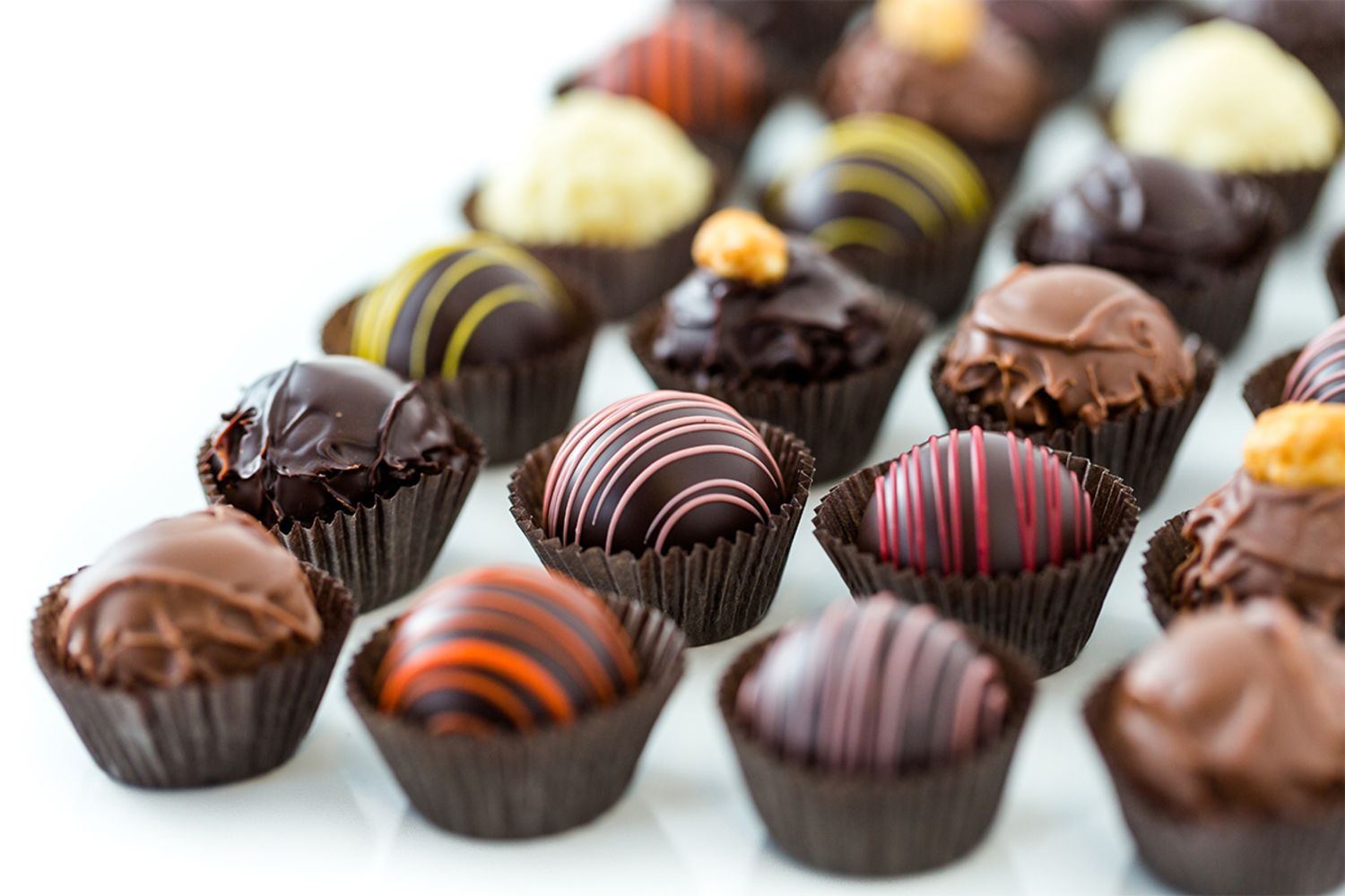 An assortment of gourmet chocolate truffles in brown paper cups, crafted with care and precision—like those made using Brown & Haley: Confectionery Equipment Auction Featuring Savage Bros Fire Mixers and more—arranged in rows on a white surface.