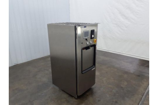 A stainless steel industrial machine with a digital display and control buttons stands on a concrete floor in a plain, white-walled room—ideal for any Bio Tech Laboratory Equipment Auction.