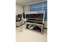 A large laboratory automation machine from the Accelerated Analytical Laboratories: Premium Laboratory Equipment Auction stands on a rolling cart in a clean, bright room, complete with a computer monitor and various equipment beneath the workstation.