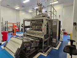 A large, industrial Premium Nutraceutical Processing and Packaging Solutions: Liquid Stick Pack Filling Mpac Langen machine stands in a clean, brightly lit lab with blue flooring and shelves in the background.