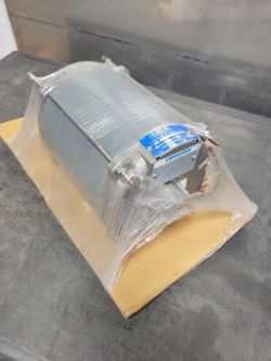A cylindrical metal blower fan wrapped in plastic sits on a piece of cardboard, placed on a dark surface. The fan, ideal for Industrial MRO Auction - Automation Parts applications, features a blue and white label on one end.