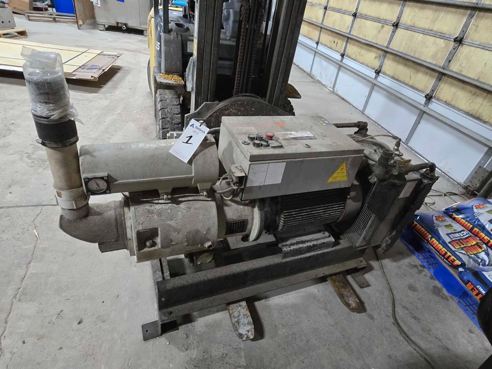 Industrial pump or motor unit mounted on a metal frame, positioned on a concrete floor near a forklift and packaged materials—part of the Snack Food and Ingredients Processing and Packaging Equipment Auction—inside a warehouse with metal and wooden panel walls.