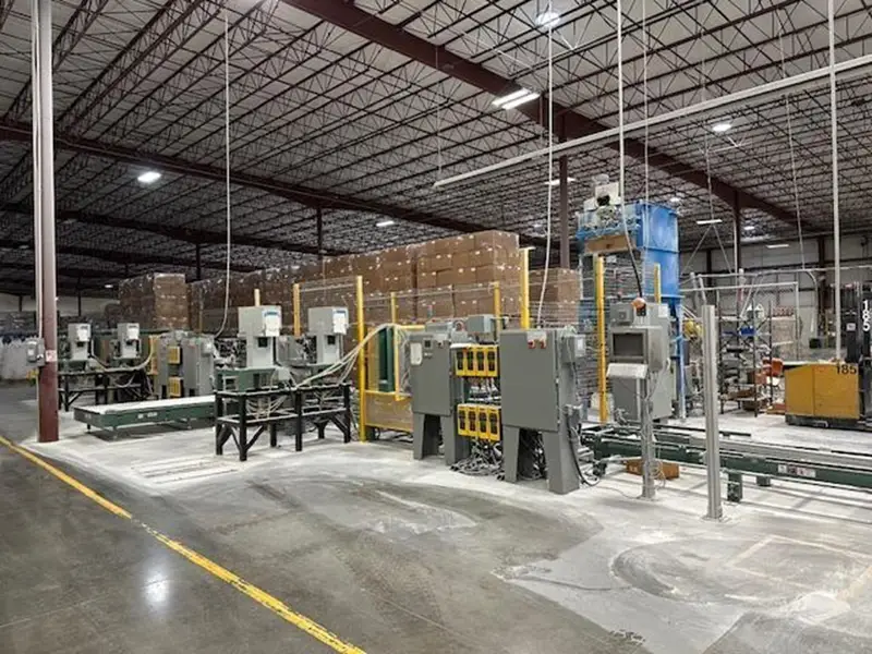 A large industrial warehouse interior with automated machinery, conveyor belts, and stacked cardboard boxes in the background showcases PPT Research: Plant Support Equipment and Laboratory Equipment Sale under a high ceiling with exposed beams and yellow safety lines.